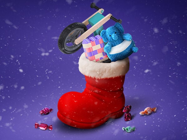 Sviatočná vianočná scéna s veľkou červenou topánkou s bielym kožušinovým lemom, plnou darčekov na fialovom zasneženom pozadí. V topánke je malé drevené odrážadlo, modrý plyšový slon a farebná sada stavebných kociek pre deti. Okolo topánky na zasneženom povrchu sú rozhádzané farebne zabalené cukríky. Vzduchom padajú snehové vločky.